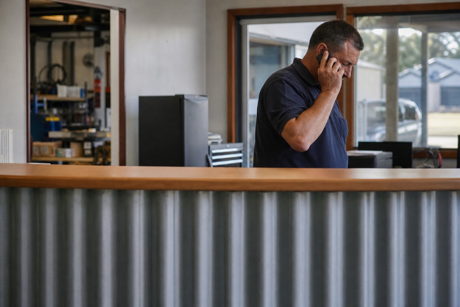 The front counter of a small Australian business, someone behind it finishing a phone call in an ordinary lived-in reception area.